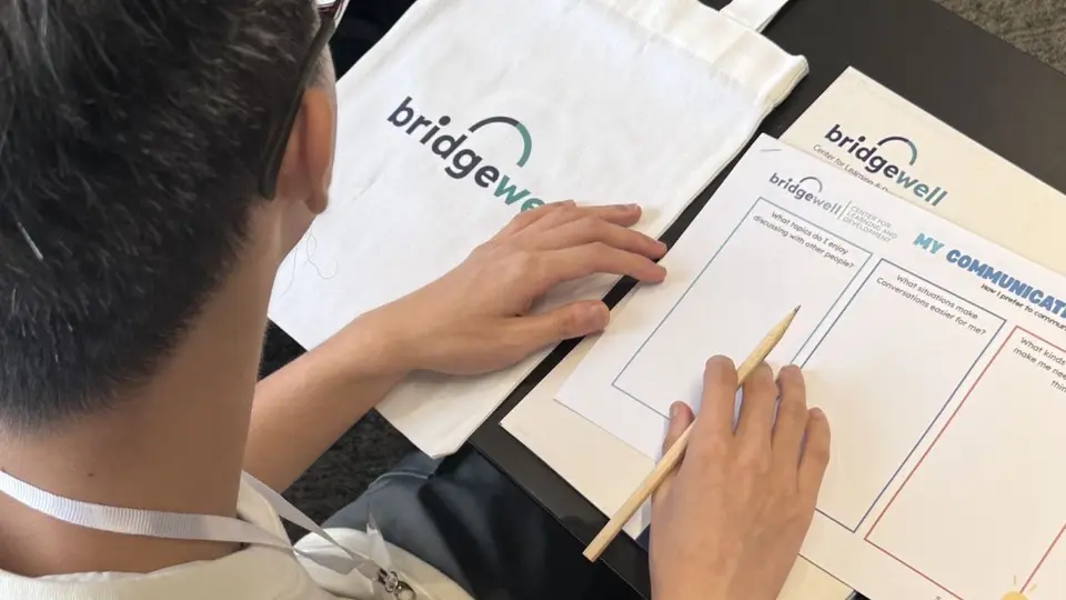 Learner working on a Bridgewell communication worksheet beside a branded tote.